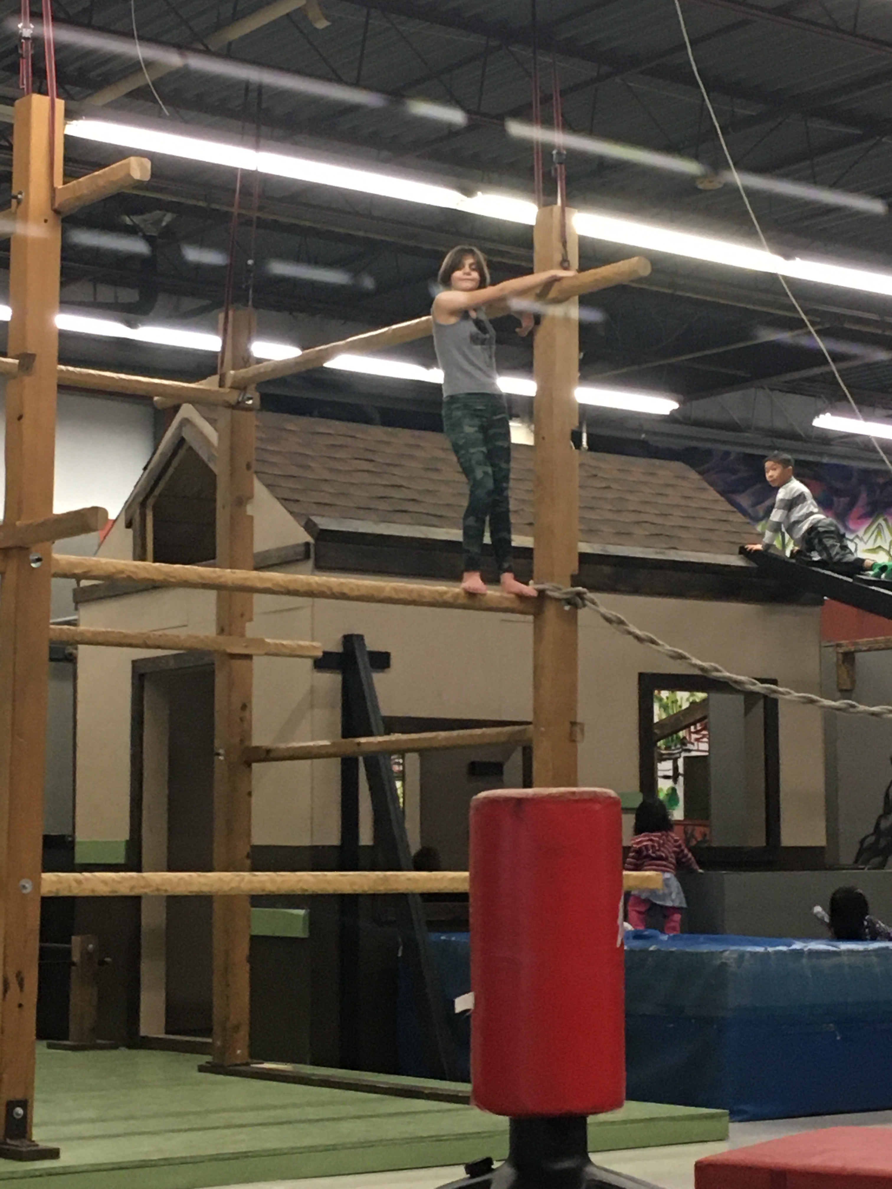 R standing on a wooden beam about nine feet in the air. She's holding onto a nearby post.