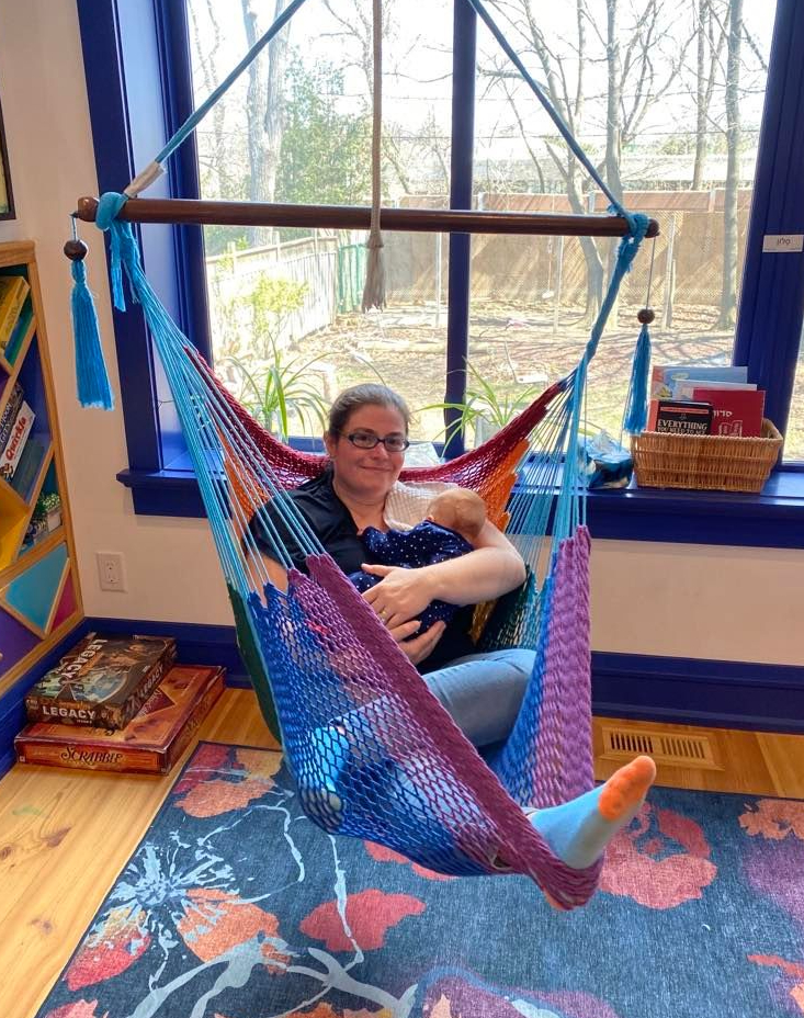 Photo of me sitting in a hammock chair, holding a baby.