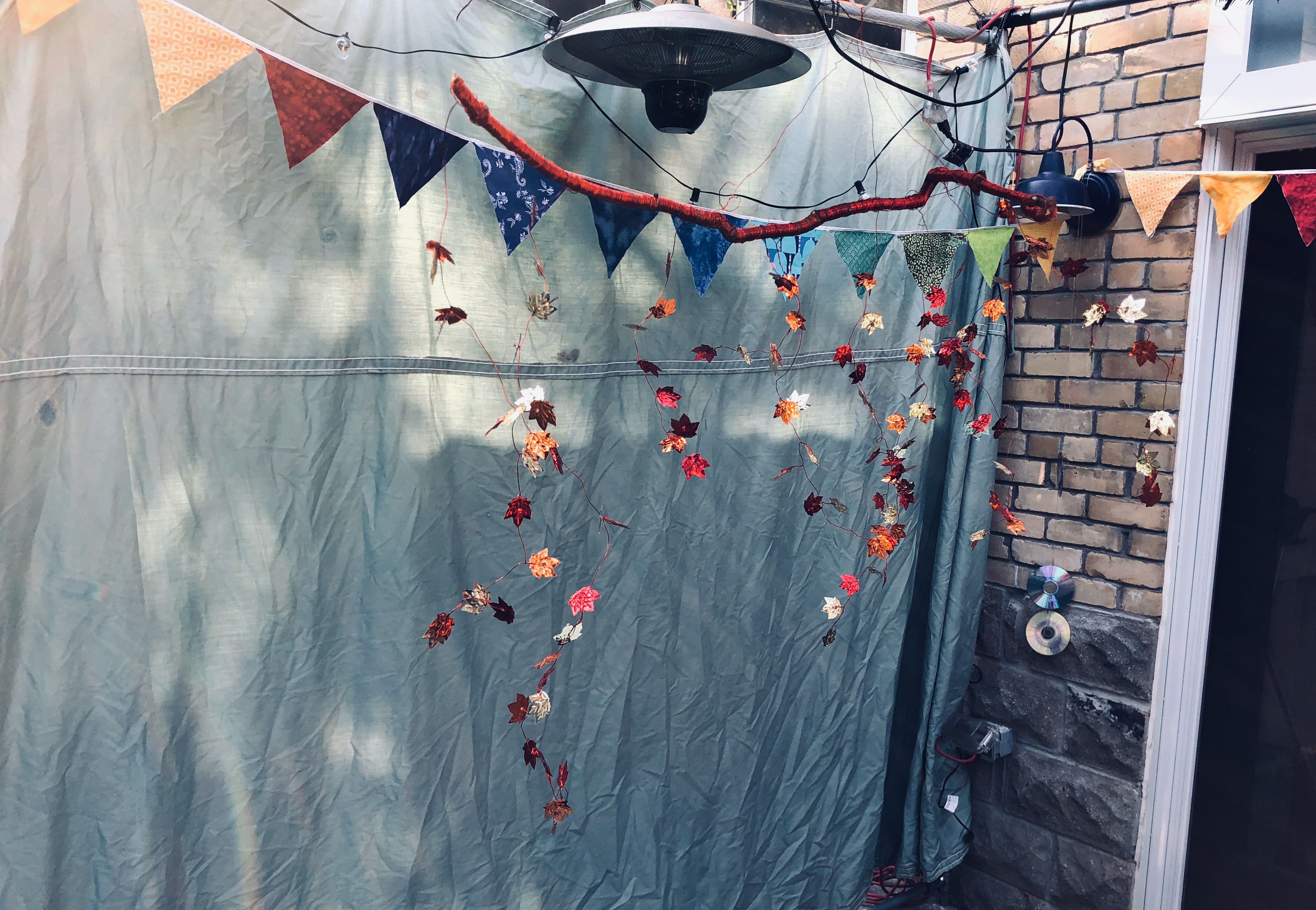 Inside the sukkah: canvas wall, fabric bunting, string lights, and a mobile made of metallic foil maple leaves and a wire-wrapped tree branch.