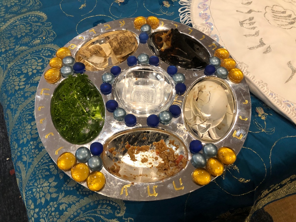 A silver-coloured seder plate with coloured flat marbles decorating it.